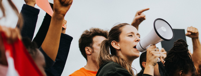 Woman speaking into megaphone surrounded by people at an outdoor protest