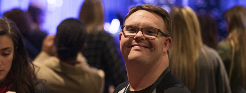 An attendee from The Arc's convention smiles with a crowd of people behind him