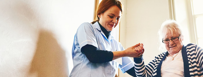 Woman caregiver helping an older woman walk down the stairs