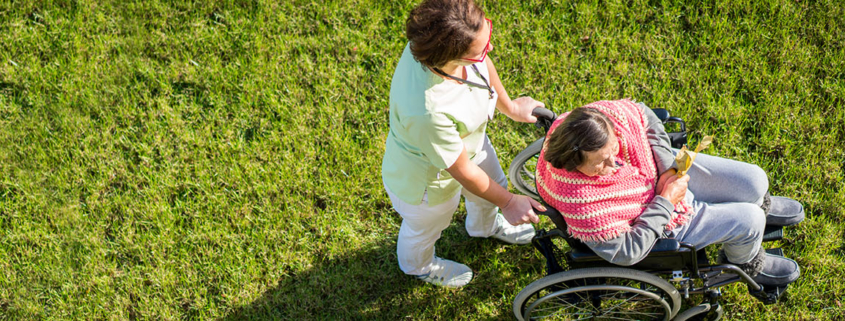 Aerial photograph of a caregiver pushing a woman in a wheelchair over grass