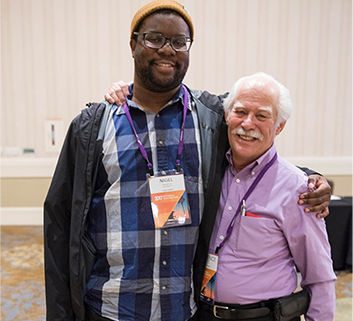 Two event attendees stand smiling with their arms around each other's shoulders.