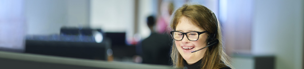 A young woman in an office setting wearing a head set and glasses