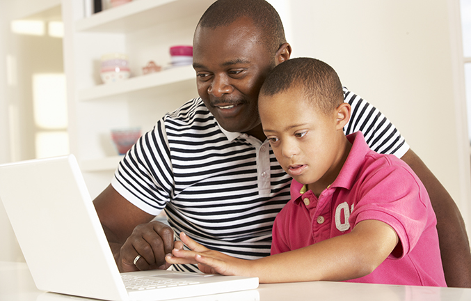 Man sitting with child with Down Syndrome using laptop