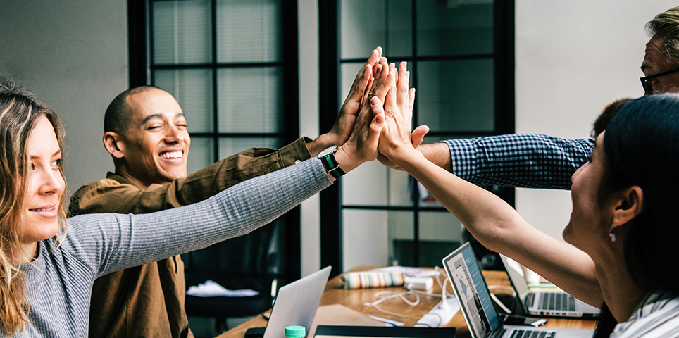 Four people in office setting high-fiving and smiling