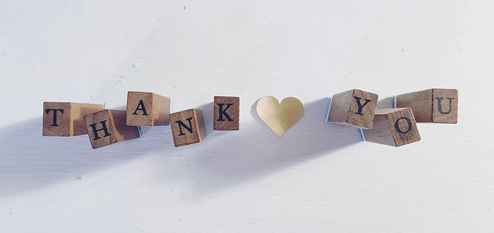 Wooden blocks on white table with letters that spell "Thank" and "you" - tan paper heart between words