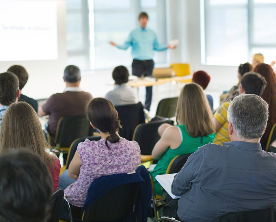 An instructor stands out of focus teaching a class of adults with their backs to the camera