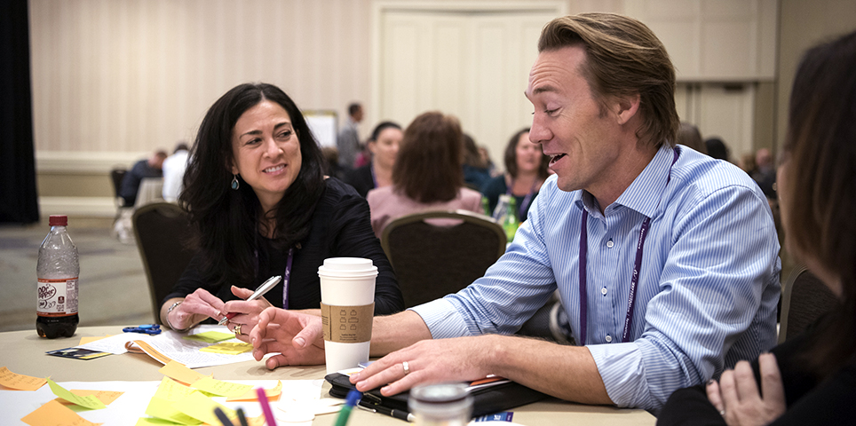 Three Summer Leadership Institute attendees sitting at a table with post-it notes and papers dispersed, deep in conversation