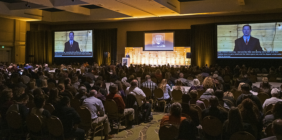 Rows of people sitting in chairs in a meeting room at The Arc's National Convention, watching Andrew Solomon speak on stage in background