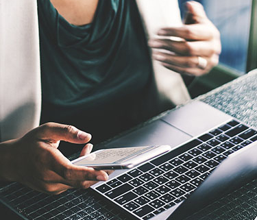 Person sitting in front of open computer, and also holding phone in their right hand