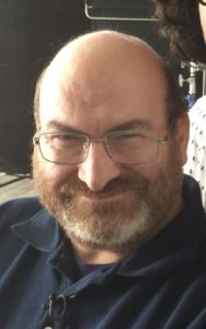 James Meadours smiles at the camera in a selfie, wearing a navy blue polo shirt and glasses.