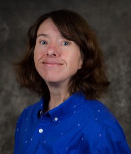 Kecia Weller poses for a photo against a gray mottled background with a blue shirt on.