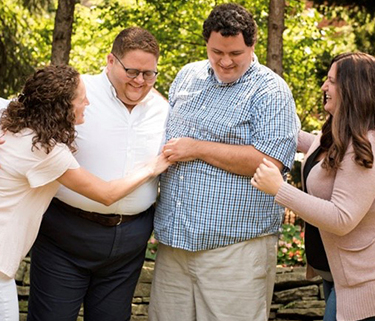 Four siblings smile and link arms together, smiling at each other