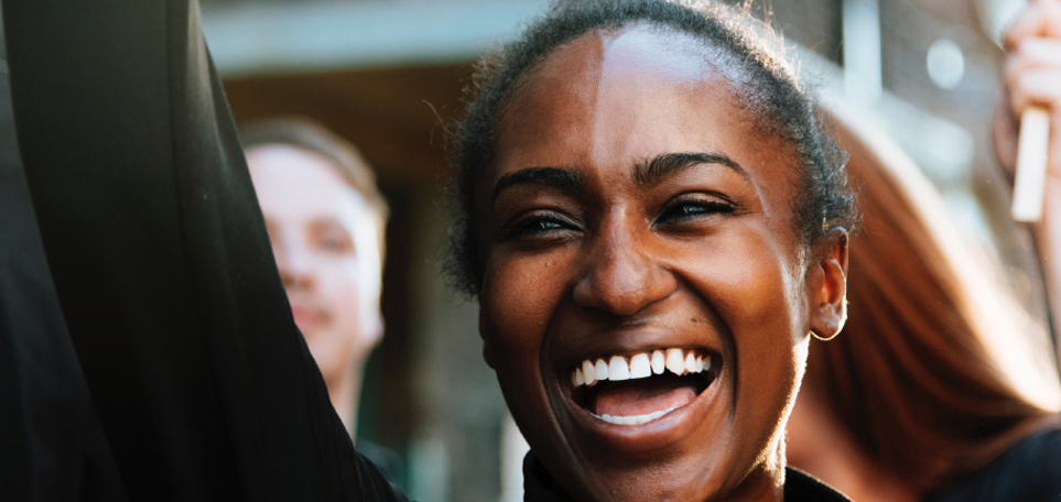 A close up of a woman's face smiling as others are blurred in the background.