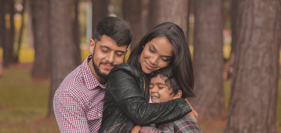 A mom, dad and son are all hugging. In the background is a forest