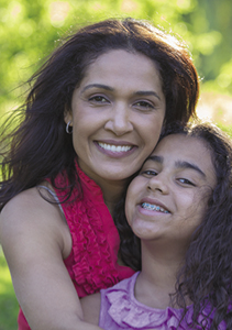 A photo of a mom and daughter. The mom is holding her daughter outside and their cheeks are touching.