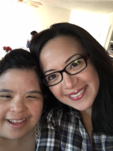 A close up of two sisters stand close to each other, looking at the camera and smiling.