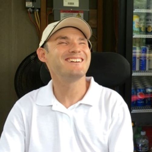 A man in a white collared shirt and a white hat smiles with his eyes closed