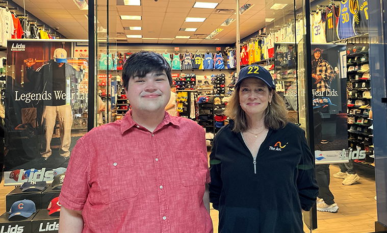 Two shoppers stand in front of a Lids store, one wearing a lids hat and a sweatshirt with The Arc's logo